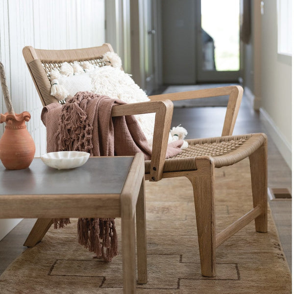 White flower shaped carved marble bowl sitting on an end table next to a wood and cane scandinavian style chair