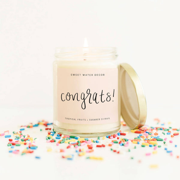 Fun gift candle in tropical fruit scent blend. Attractive calligraphy script Congrats! sentiment on blush colored label over clear glass jar with gold lid.