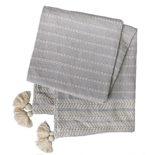 Handwoven gray cotton throw with cream stripe and chevron accents, finished with tassels at each corner.